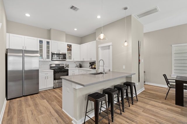 413 Stonework Oaks Ln, Houston, TX 77076 - kitchen featuring appliances with stainless steel finishes, a kitchen bar, light wood-style floors, backsplash, and glass insert cabinets