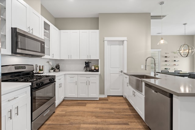 413 Stonework Oaks Ln, Houston, TX 77076 - kitchen with stainless steel appliances, a peninsula, wood finished floors, white cabinetry, and a chandelier