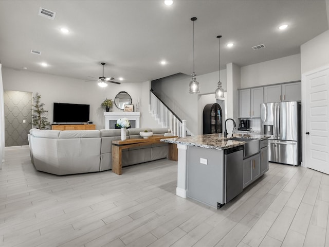 706 Westwood Dr, League City, TX 77573 - kitchen with appliances with stainless steel finishes, gray cabinetry, light stone countertops, ceiling fan, and a kitchen island with sink