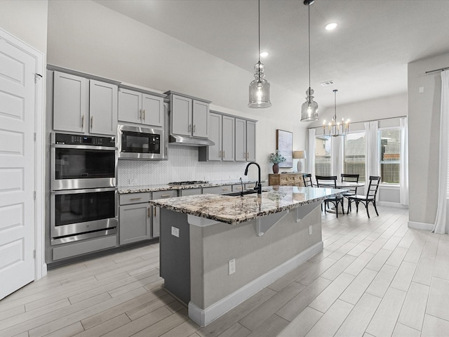 706 Westwood Dr, League City, TX 77573 - kitchen featuring gray cabinets, appliances with stainless steel finishes, light stone countertops, backsplash, and light wood-style floors