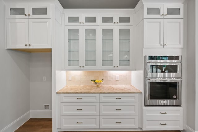 161 Pine Branch Dr, Montgomery, TX 77356 - kitchen with double oven, light stone counters, dark wood-style flooring, white cabinetry, and glass insert cabinets