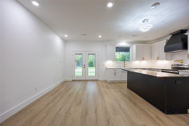 51 V Allen Ln, Coldspring, TX 77331 - kitchen with stainless steel range with electric stovetop, premium range hood, white cabinetry, light wood-style flooring, and light countertops