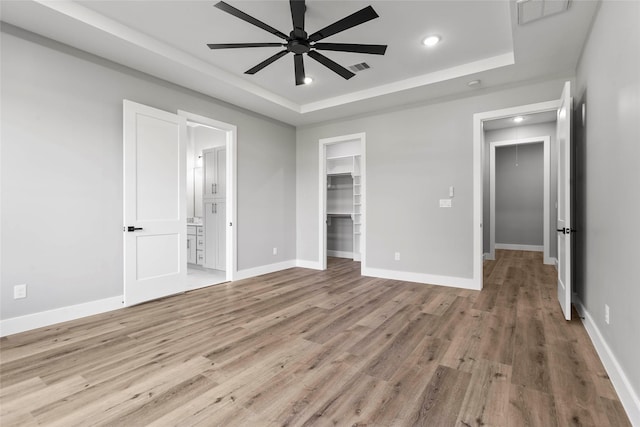 210 Hogan Ln, Hempstead, TX 77445 - unfurnished bedroom with a tray ceiling, light wood-type flooring, a spacious closet, recessed lighting, and ensuite bathroom