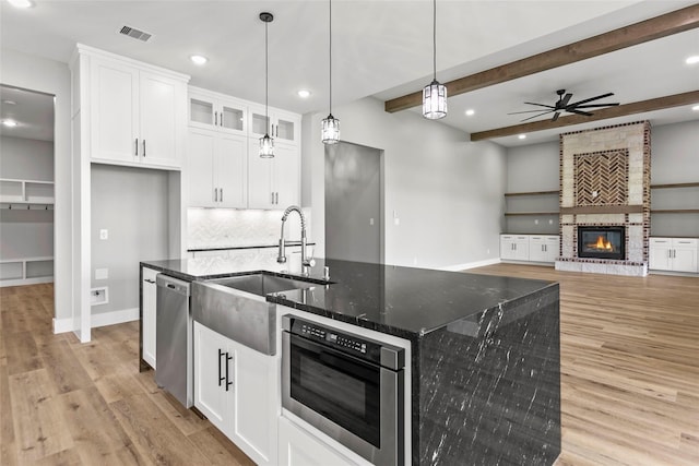 210 Hogan Ln, Hempstead, TX 77445 - kitchen featuring dishwasher, backsplash, light wood-style floors, dark stone countertops, and an island with sink