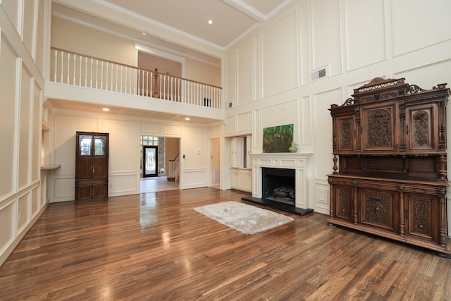 9327 Tranquil Park Dr, Spring, TX 77379 - unfurnished living room featuring a decorative wall, crown molding, a towering ceiling, dark wood-style floors, and a fireplace with raised hearth