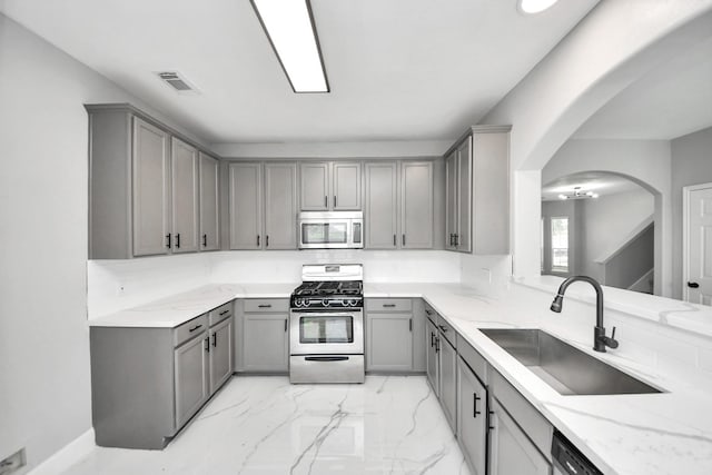 7427 Oakwood Canyon Dr, Cypress, TX 77433 - kitchen with gray cabinetry, stainless steel appliances, arched walkways, light marble finish floors, and light stone countertops