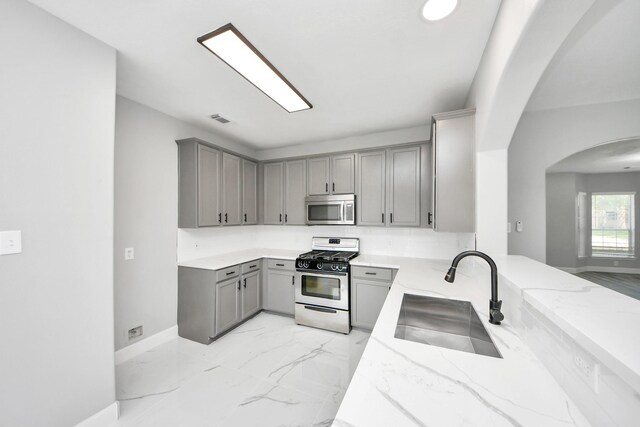 7427 Oakwood Canyon Dr, Cypress, TX 77433 - kitchen featuring stainless steel appliances, gray cabinetry, arched walkways, and light stone countertops