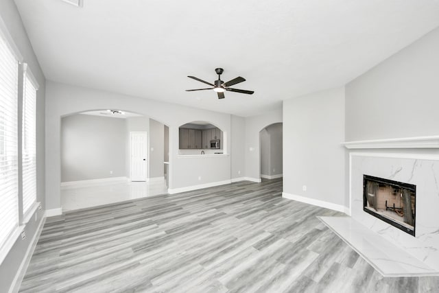 7427 Oakwood Canyon Dr, Cypress, TX 77433 - unfurnished living room with a ceiling fan, arched walkways, light wood-type flooring, and a high end fireplace