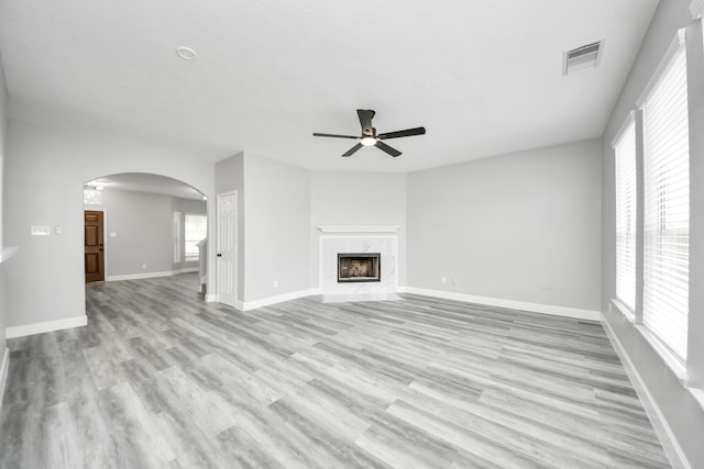 7427 Oakwood Canyon Dr, Cypress, TX 77433 - unfurnished living room featuring ceiling fan, arched walkways, light wood-style flooring, and a high end fireplace