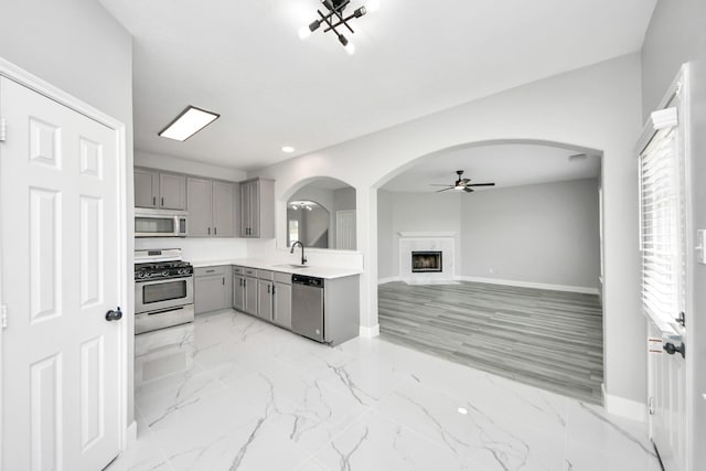 7427 Oakwood Canyon Dr, Cypress, TX 77433 - kitchen with gray cabinets, stainless steel appliances, ceiling fan, arched walkways, and a fireplace