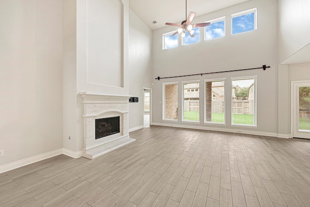 20010 Barrow Edge Ln, Cypress, TX 77433 - unfurnished living room with a ceiling fan, high vaulted ceiling, light wood-style floors, a fireplace with raised hearth, and plenty of natural light