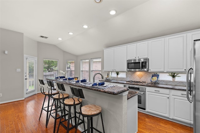 99 E Foxbriar Forest Cir, The Woodlands, TX 77382 - kitchen featuring appliances with stainless steel finishes, decorative backsplash, white cabinets, light wood finished floors, and lofted ceiling