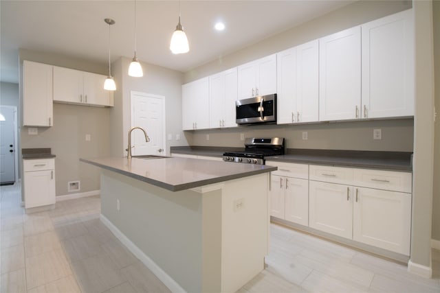 324 Gans St Unit B, Houston, TX 77029 - kitchen featuring appliances with stainless steel finishes, dark countertops, white cabinetry, an island with sink, and hanging light fixtures