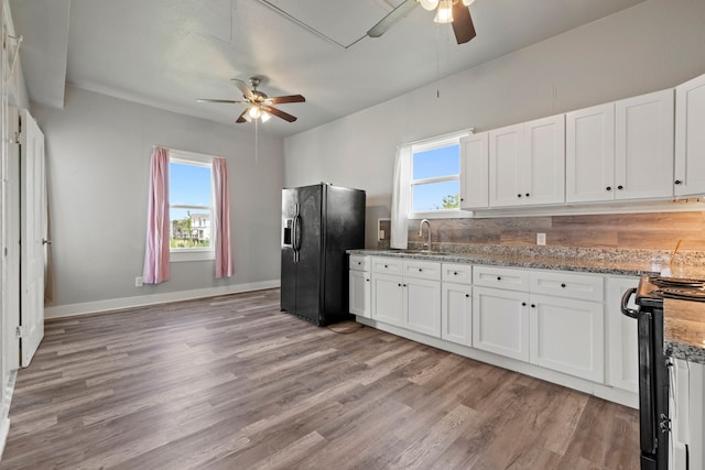 2714 Ball St, Galveston, TX 77550 - kitchen with black fridge with ice dispenser, a ceiling fan, gas stove, and white cabinets