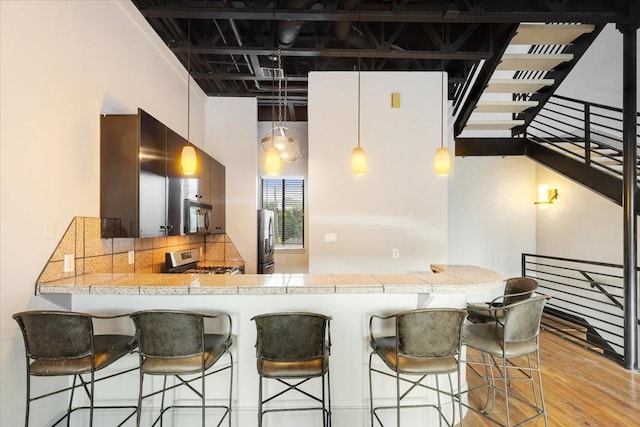 1020 Columbus St, Houston, TX 77019 - kitchen with appliances with stainless steel finishes, light wood finished floors, a peninsula, a breakfast bar, and pendant lighting