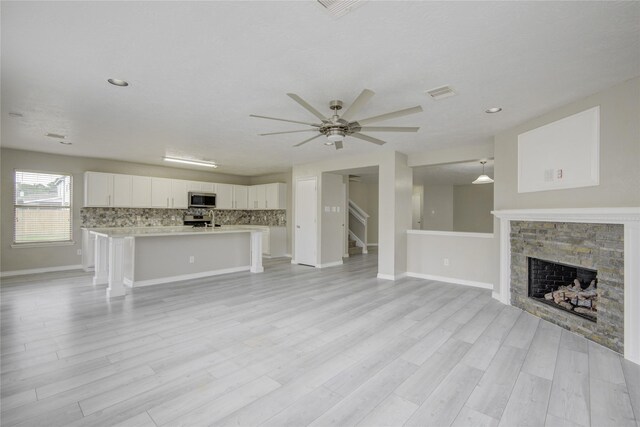 7255 Liberty Mesa Ln, Houston, TX 77049 - unfurnished living room with a stone fireplace, ceiling fan, light wood finished floors, stairs, and recessed lighting