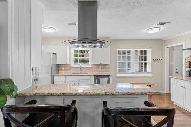 32047 S Wiggins St, Magnolia, TX 77355 - kitchen with stainless steel appliances, island range hood, white cabinetry, a kitchen breakfast bar, and tasteful backsplash