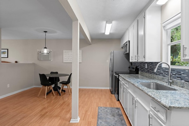 32047 S Wiggins St, Magnolia, TX 77355 - kitchen featuring black electric range oven, stainless steel microwave, light wood-style flooring, and white cabinets