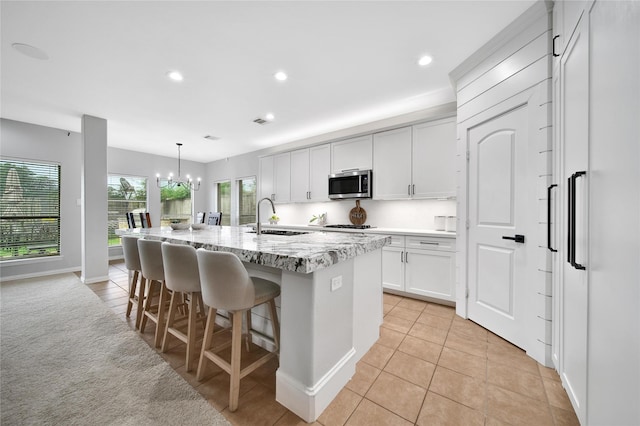 14314 Prosper Ridge Dr, Cypress, TX 77429 - kitchen with stainless steel microwave, a center island with sink, a chandelier, a breakfast bar area, and white cabinets