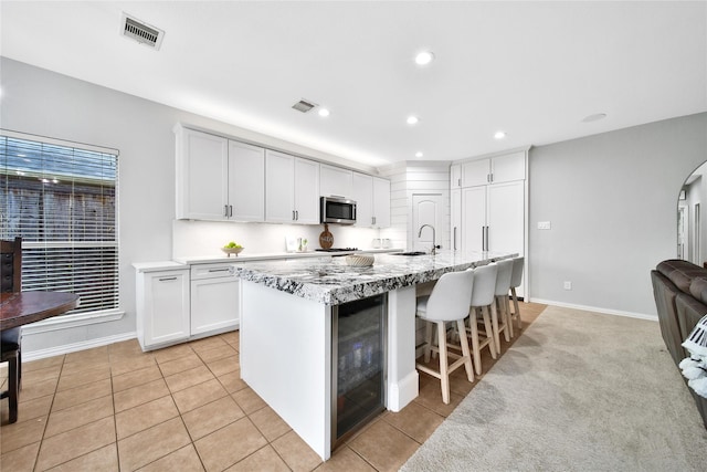 14314 Prosper Ridge Dr, Cypress, TX 77429 - kitchen with stainless steel microwave, beverage cooler, light tile patterned flooring, white cabinetry, and an island with sink