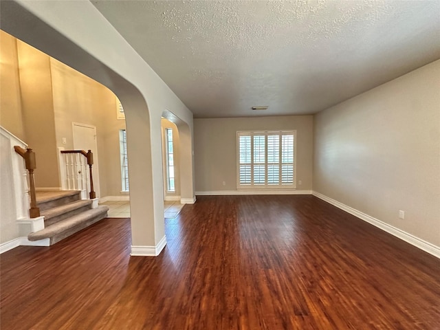 12807 Stratford Heights Dr, Sugar Land, TX 77498 - unfurnished living room featuring arched walkways, dark wood finished floors, a textured ceiling, and stairway