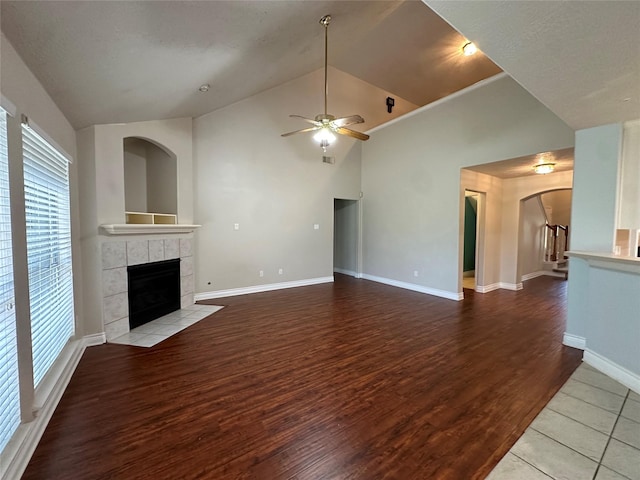 12807 Stratford Heights Dr, Sugar Land, TX 77498 - unfurnished living room with a tiled fireplace, a ceiling fan, arched walkways, wood finished floors, and high vaulted ceiling