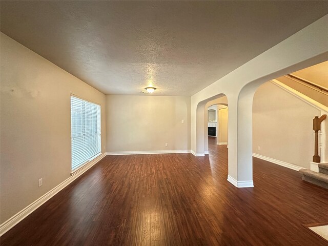 12807 Stratford Heights Dr, Sugar Land, TX 77498 - unfurnished room with dark wood-style floors, stairs, arched walkways, and a textured ceiling