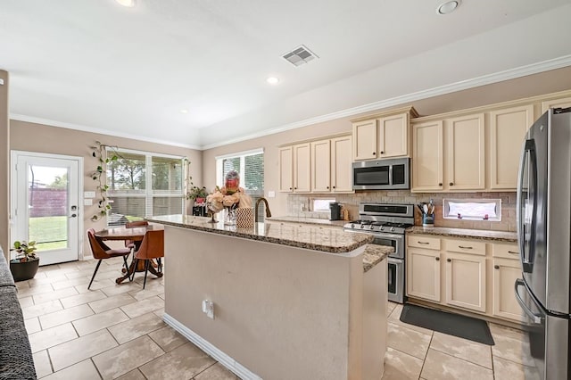 19443 Alton Springs Dr, Cypress, TX 77433 - kitchen with appliances with stainless steel finishes, cream cabinets, a center island with sink, backsplash, and light stone countertops