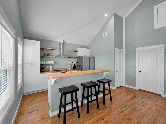 1032 Sunset Cir W, Crystal Beach, TX 77650 - kitchen featuring butcher block countertops, freestanding refrigerator, wall chimney exhaust hood, open shelves, and a breakfast bar