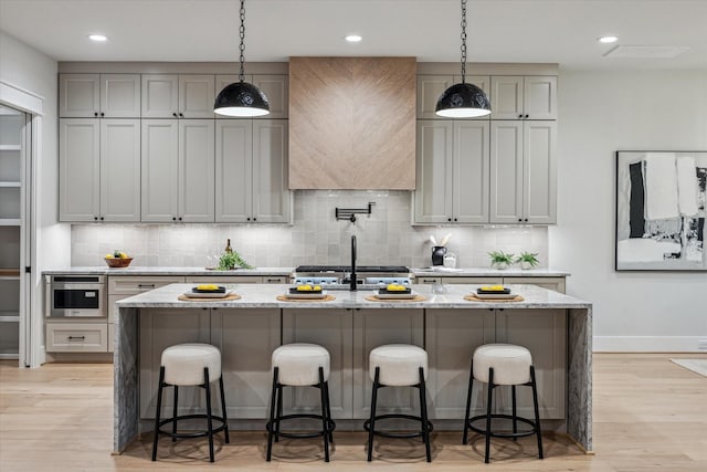 608 E 25th St, Houston, TX 77008 - kitchen with backsplash, light wood-style floors, a center island with sink, light stone counters, and recessed lighting