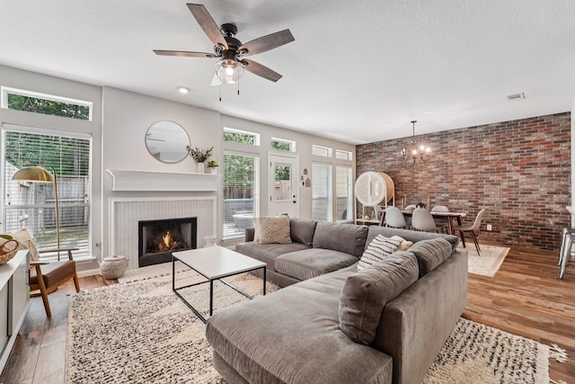 87 E Greenhill Terrace Pl, The Woodlands, TX 77382 - living room featuring brick wall, a ceiling fan, a tiled fireplace, wood finished floors, and a chandelier