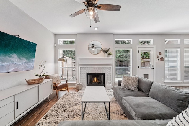 87 E Greenhill Terrace Pl, The Woodlands, TX 77382 - living area featuring a ceiling fan, dark wood-style flooring, and a warm lit fireplace