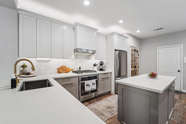 87 E Greenhill Terrace Pl, The Woodlands, TX 77382 - kitchen featuring appliances with stainless steel finishes, dark wood-type flooring, light countertops, decorative backsplash, and extractor fan