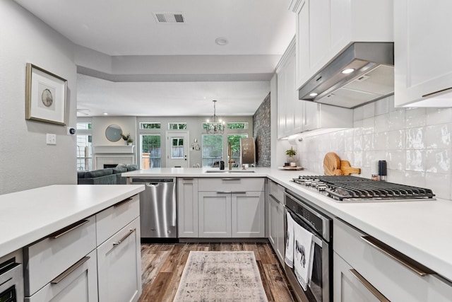 87 E Greenhill Terrace Pl, The Woodlands, TX 77382 - kitchen featuring appliances with stainless steel finishes, dark wood-type flooring, light countertops, open floor plan, and a peninsula