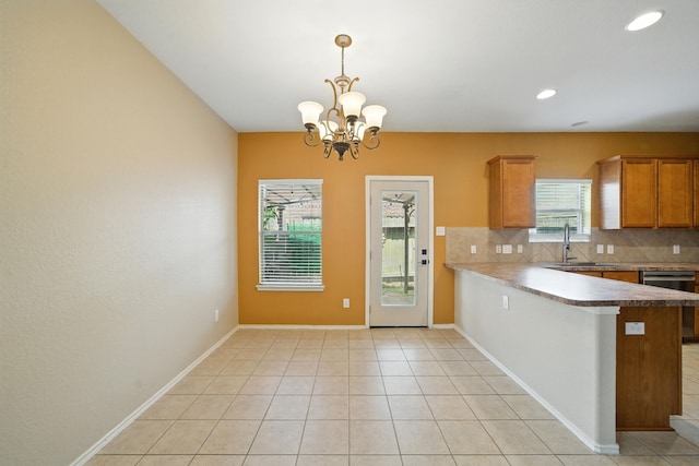 18123 Hillock Glen Ln, Cypress, TX 77429 - kitchen with stainless steel dishwasher, tasteful backsplash, brown cabinets, a peninsula, and a chandelier