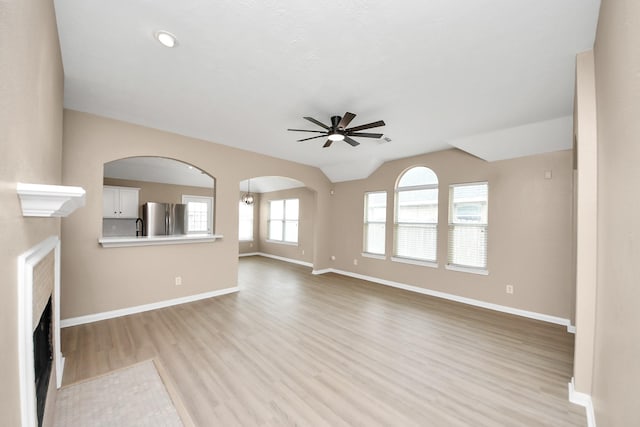 7407 Rustic Chase Dr, Richmond, TX 77407 - unfurnished living room featuring ceiling fan, light wood-style flooring, a fireplace with flush hearth, vaulted ceiling, and arched walkways