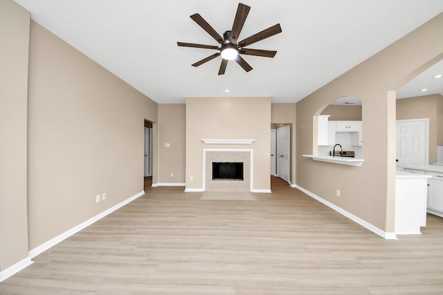 7407 Rustic Chase Dr, Richmond, TX 77407 - unfurnished living room featuring ceiling fan, light wood-style floors, a tiled fireplace, arched walkways, and recessed lighting