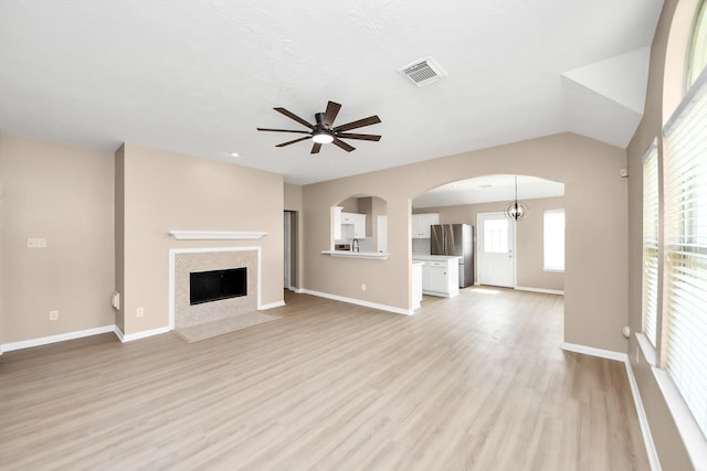 7407 Rustic Chase Dr, Richmond, TX 77407 - unfurnished living room featuring a ceiling fan, light wood-style flooring, a fireplace, arched walkways, and lofted ceiling