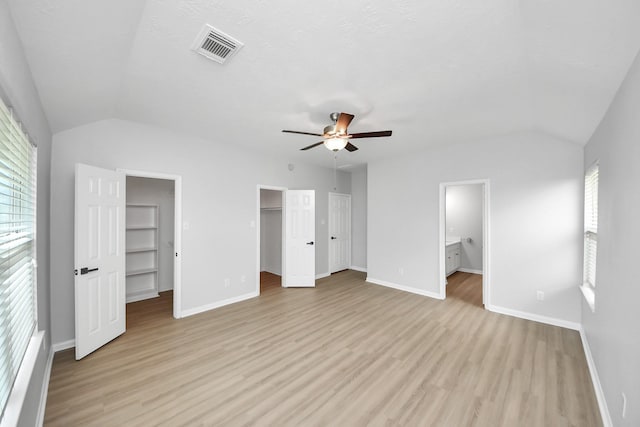 7407 Rustic Chase Dr, Richmond, TX 77407 - unfurnished bedroom with vaulted ceiling, a walk in closet, multiple windows, light wood-type flooring, and connected bathroom