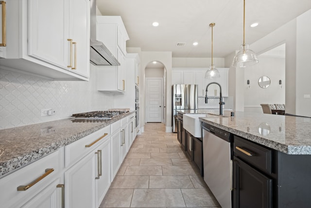 16715 Bark Cabin Dr, Humble, TX 77346 - kitchen with wall chimney range hood, appliances with stainless steel finishes, decorative backsplash, white cabinetry, and a kitchen island with sink