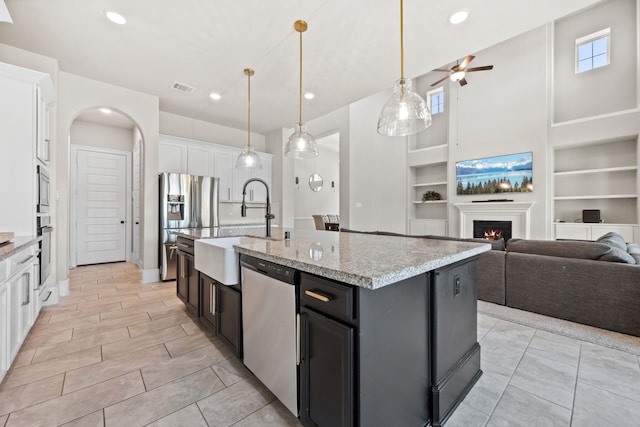 16715 Bark Cabin Dr, Humble, TX 77346 - kitchen featuring appliances with stainless steel finishes, a ceiling fan, white cabinetry, a lit fireplace, and built in features