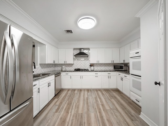 19518 Barwick Dr, Spring, TX 77373 - kitchen featuring stainless steel appliances, wall chimney exhaust hood, tasteful backsplash, light wood-style flooring, and white cabinets