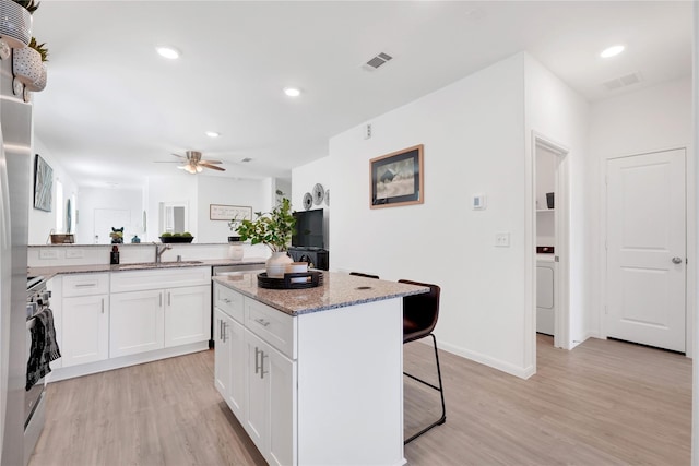23823 Escardilla Ln, Hockley, TX 77447 - kitchen with a breakfast bar area, stainless steel stove, light stone counters, white cabinets, and light wood finished floors