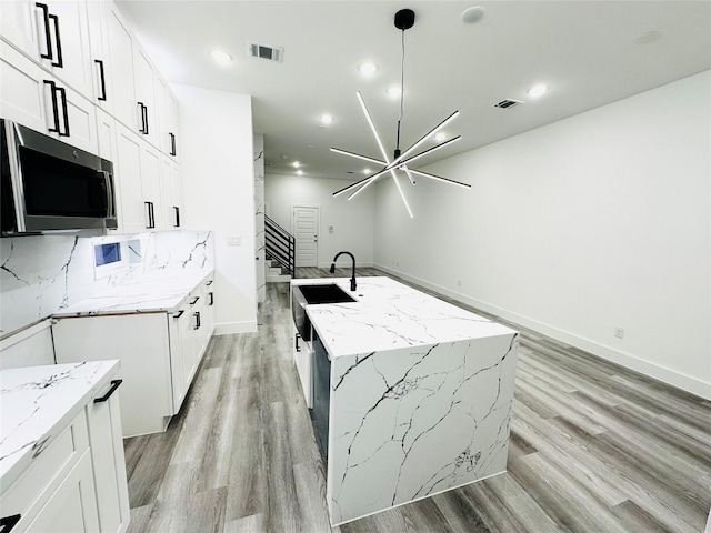 5042 Pershing St Unit Ab, Houston, TX 77033 - kitchen featuring stainless steel microwave, light wood finished floors, light stone countertops, a chandelier, and a center island with sink