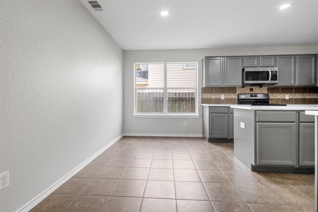9987 Sterling Place Dr, Conroe, TX 77303 - kitchen with stainless steel appliances, gray cabinetry, tasteful backsplash, tile patterned flooring, and a textured wall