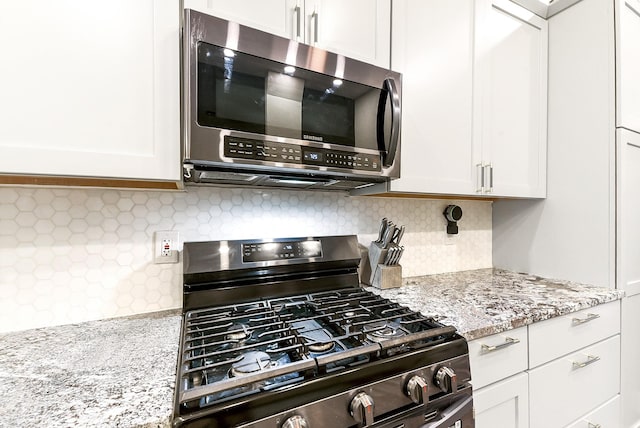 12223 Paddock Way, Houston, TX 77065 - kitchen with stainless steel microwave, range with gas cooktop, white cabinetry, light stone countertops, and decorative backsplash