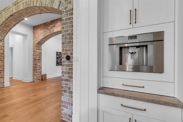 37732 Marias Way, Magnolia, TX 77354 - kitchen with arched walkways, brick wall, light wood-type flooring, stainless steel oven, and dark countertops