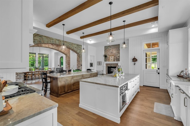 37732 Marias Way, Magnolia, TX 77354 - kitchen featuring a large island, a fireplace, arched walkways, light wood-style flooring, and beamed ceiling