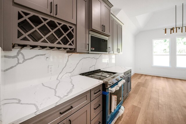 8703 Miller Rd, Magnolia, TX 77354 - kitchen featuring stainless steel gas stove, light wood-type flooring, light stone countertops, decorative backsplash, and gray cabinetry