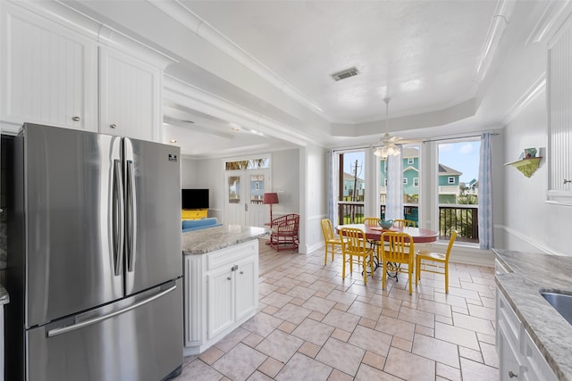 22517 Bay Point Dr, Galveston, TX 77554 - kitchen featuring freestanding refrigerator, a tray ceiling, stone tile flooring, white cabinetry, and ornamental molding